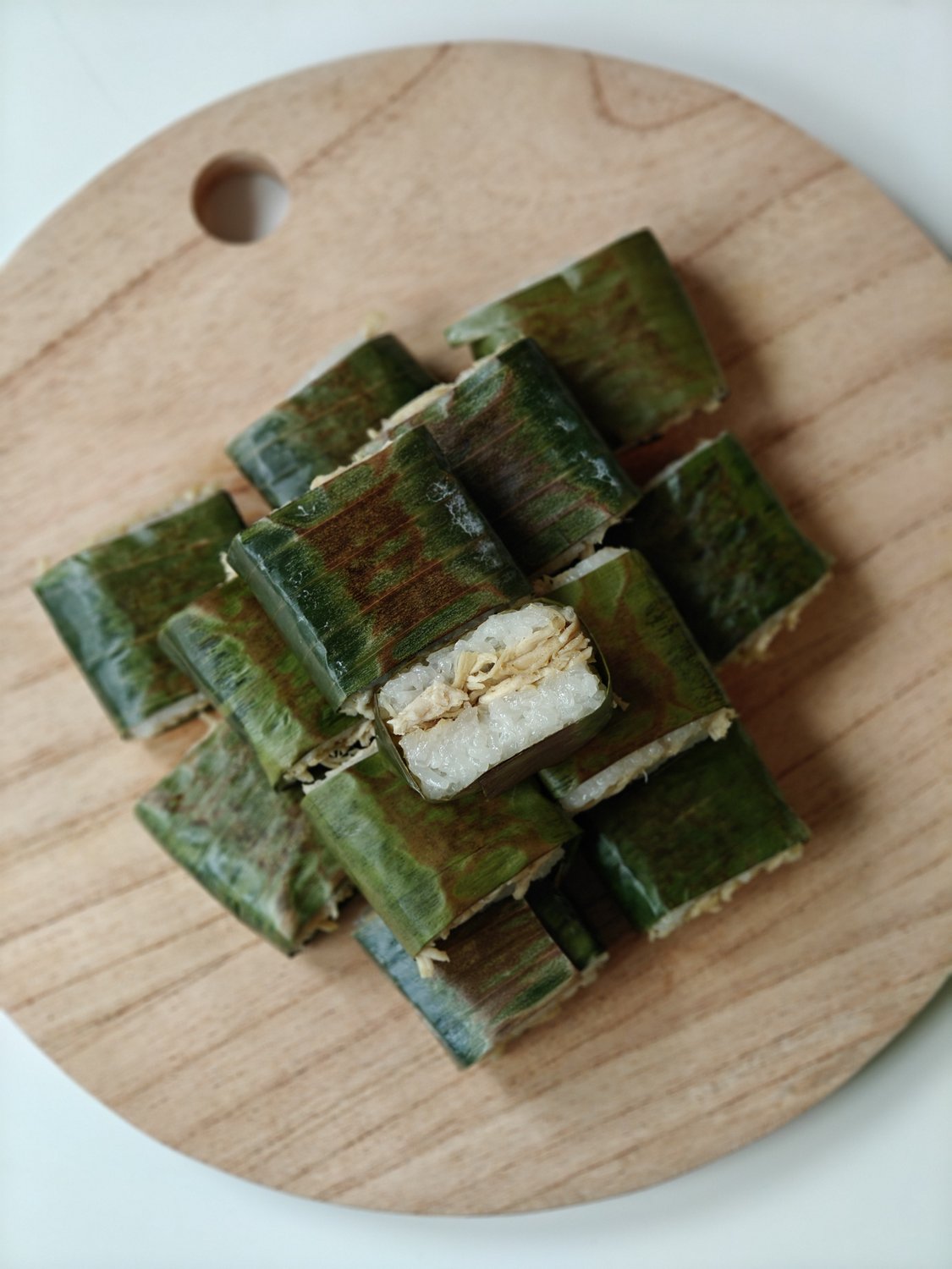 Sticky rice cakes wrapped in banana leaf, stacked to reveal shredded chicken filling